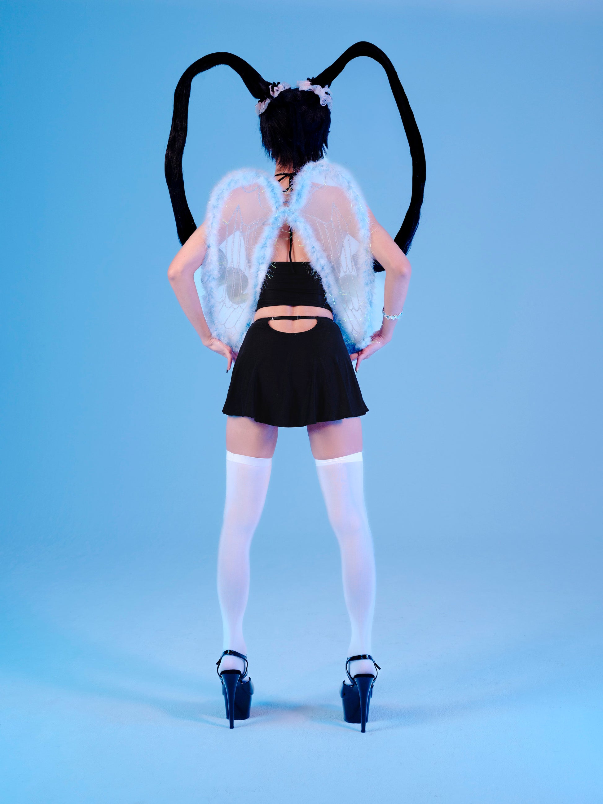 Person wearing a black outfit with angel wings and black horns on a blue background