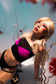Person in a costume with blonde hair and pink top, standing against a floral background.