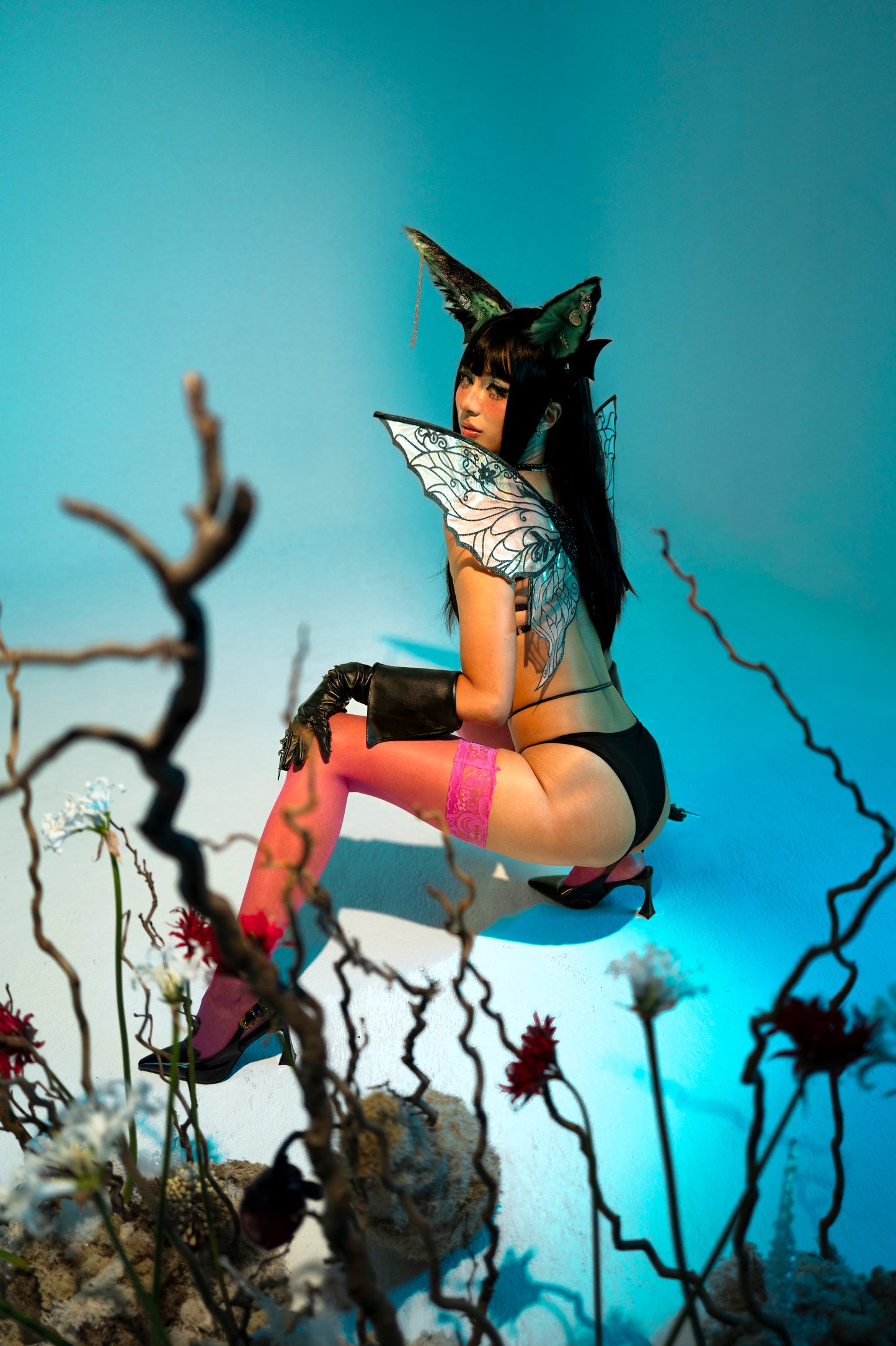 Person in fantasy costume with wings and animal ears sitting on a branch against a blue sky.
