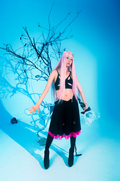 Person with pink hair and black outfit standing against a blue background