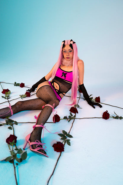 Person in cosplay with pink hair and black outfit surrounded by roses on a light blue background